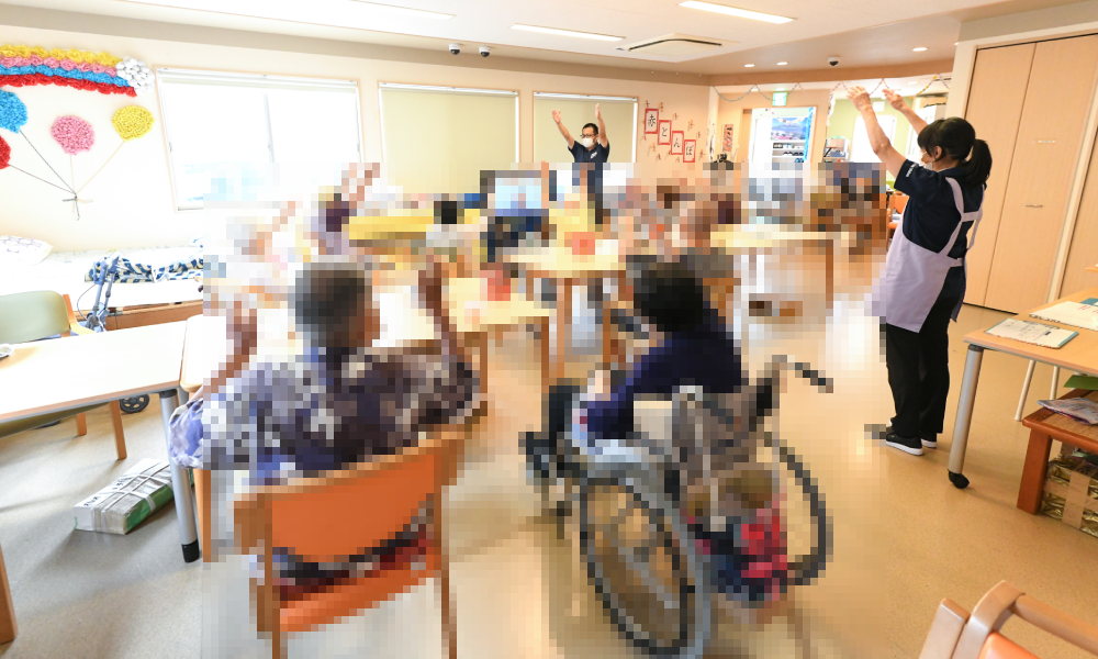 ご利用者様と職員がテレビの前で体操している様子